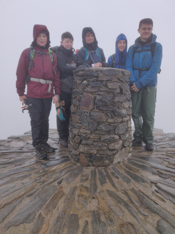 Group huddled around the summit monument of Snowdon